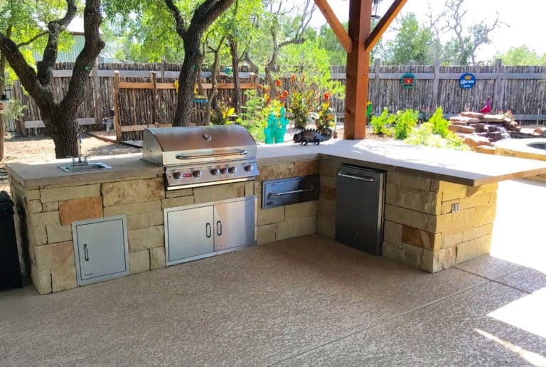Outdoor Kitchen of natural stone with sink, grill top, dutch oven and mini fridge by design and build landscaper
