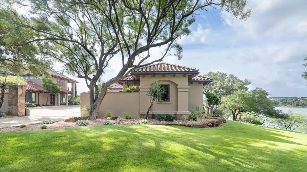 green lawn on lakefront spanish style home with gravel filled plant beds and plants native to central Texas