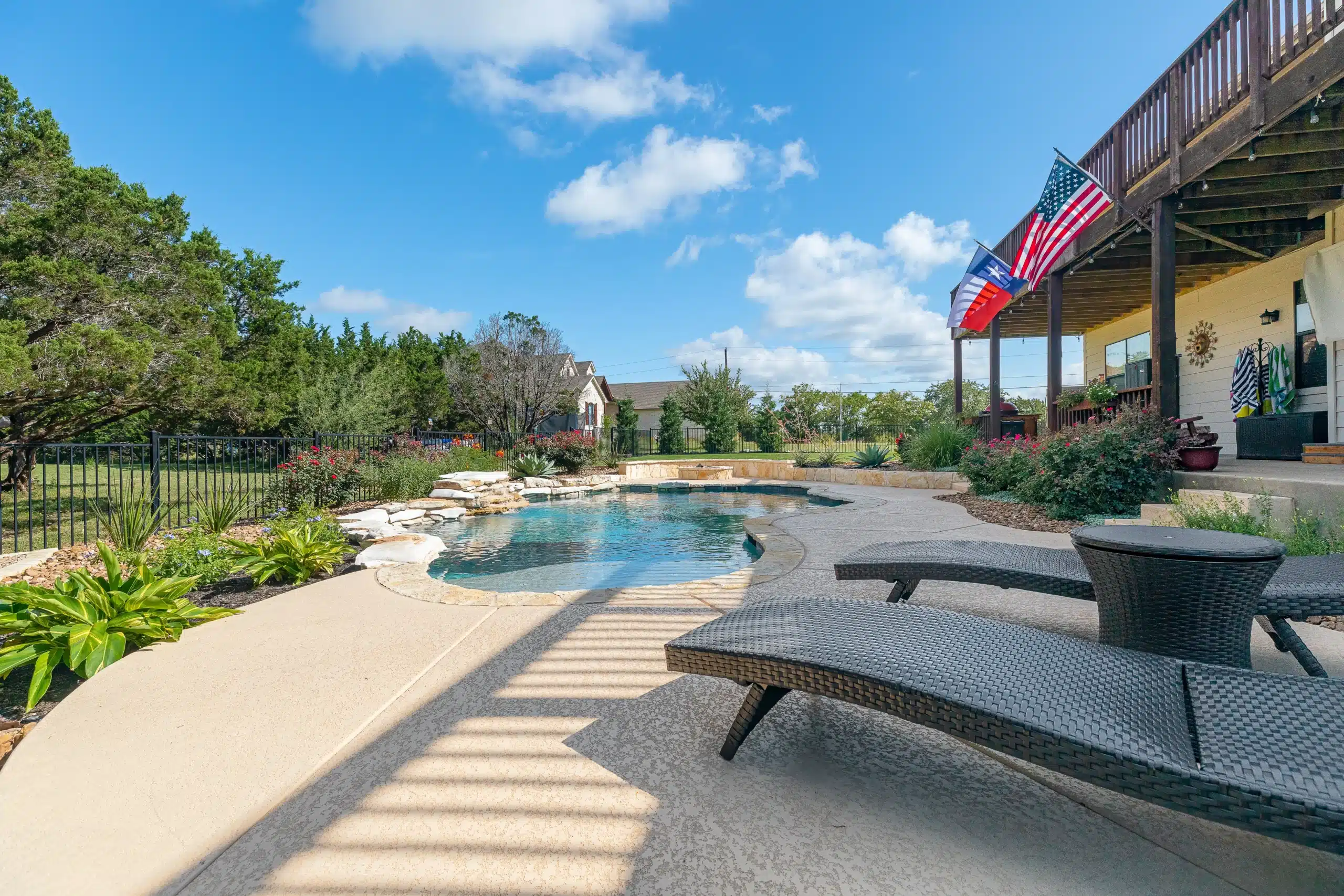 backyard with pool and lounge chairs behind two story home with deck adorned with texas and united states flags