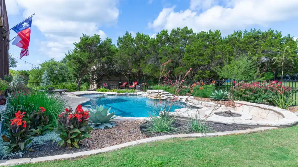 home in rural area with a lot of trees around the backyard with pool surrounded by raised plant beds of natural stone with native plants and flowers