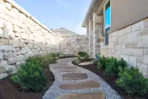 view of walkway with natural stone steps and gravel with mulch beds along the side and green shrubs in Central Texas