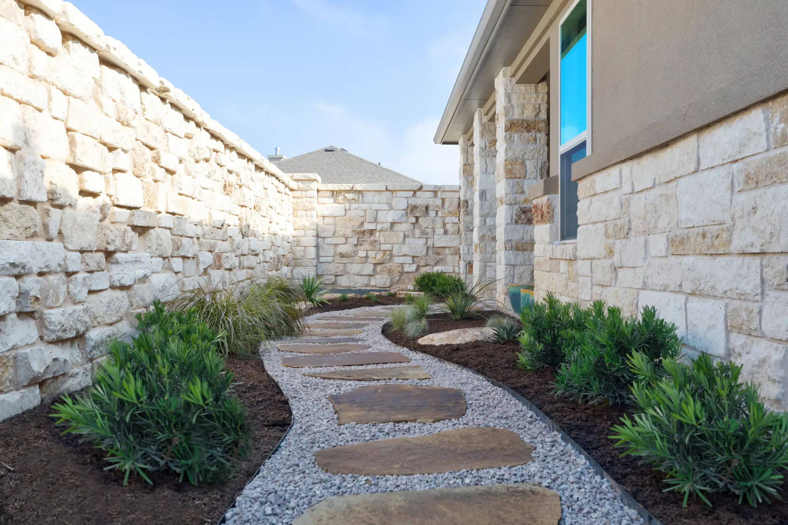 view of walkway with natural stone steps and gravel with mulch beds along the side and green shrubs in Central Texas