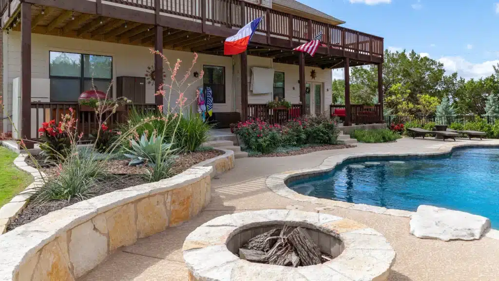 natural stone fire pit and raised plant beds with Texas-native plants around backyard in-ground pool in Liberty Hill