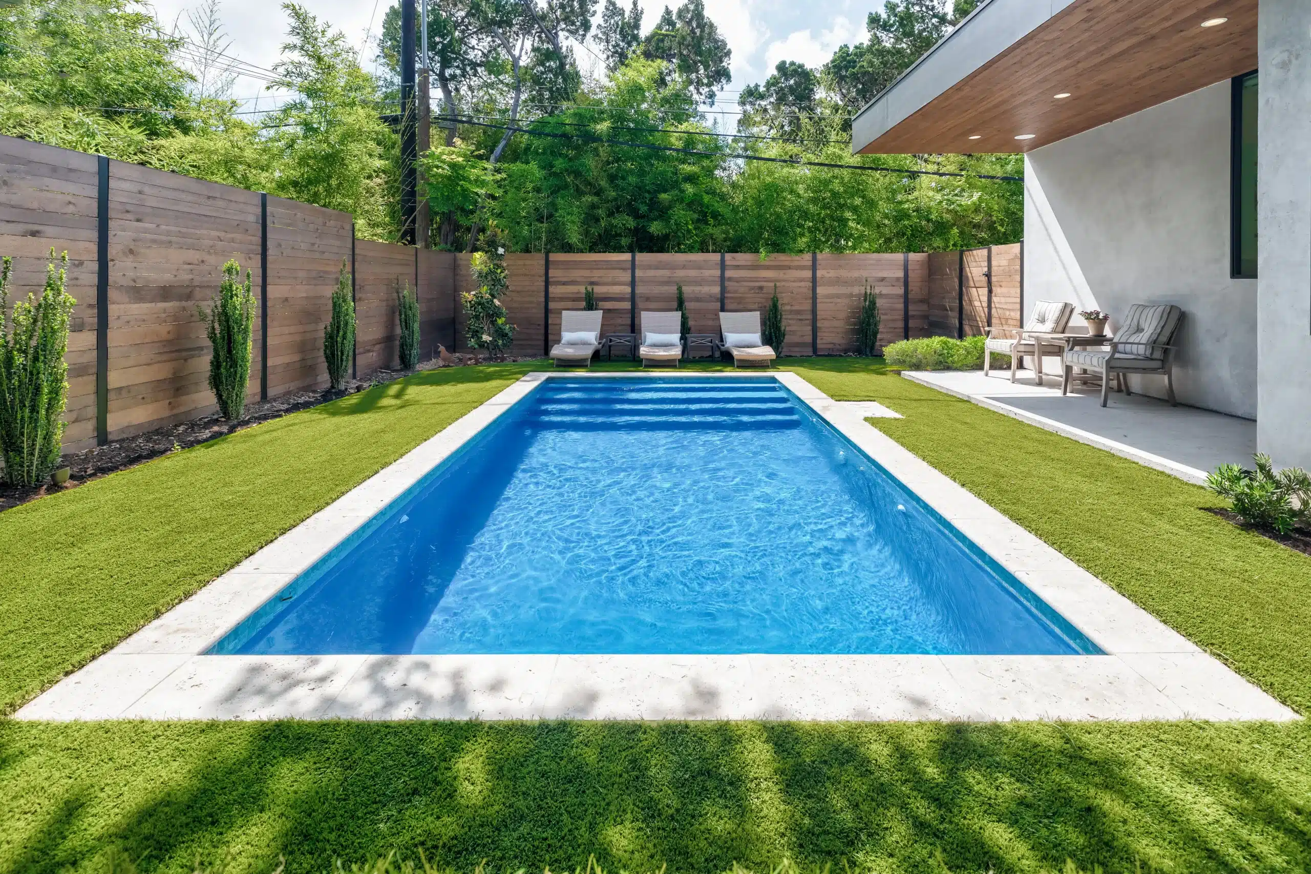 pool with clear blue water and lounge chairs surrounded by lush green grass and horizontal privacy fence