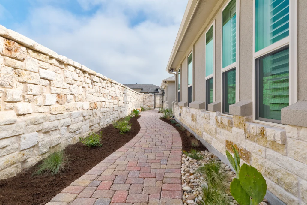 brick paver walkway along side of home lined with mulch plant beds and rock wall