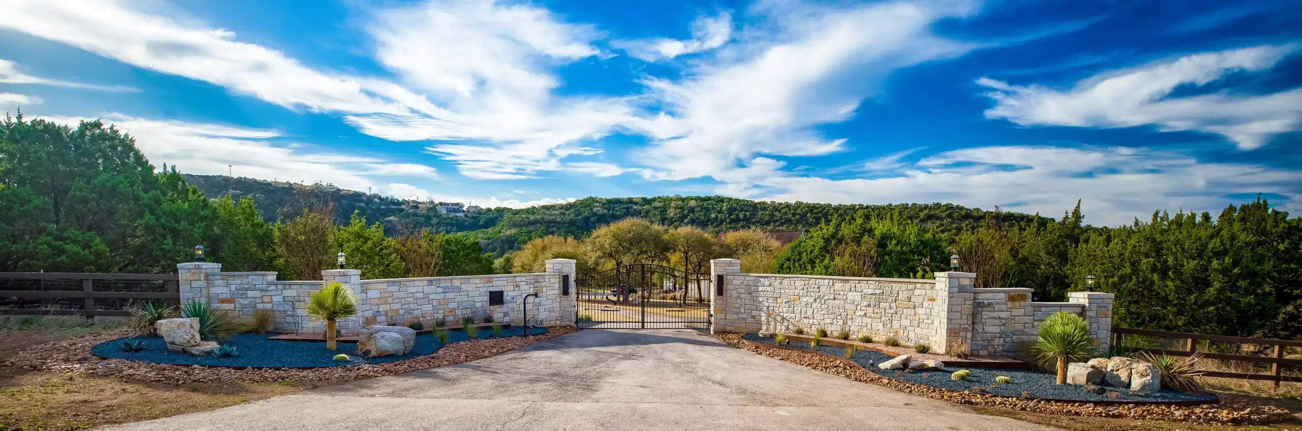 rock wall with gated entry for rural home, lined with rock-filled plant beds, natural rock and Texas-native plants