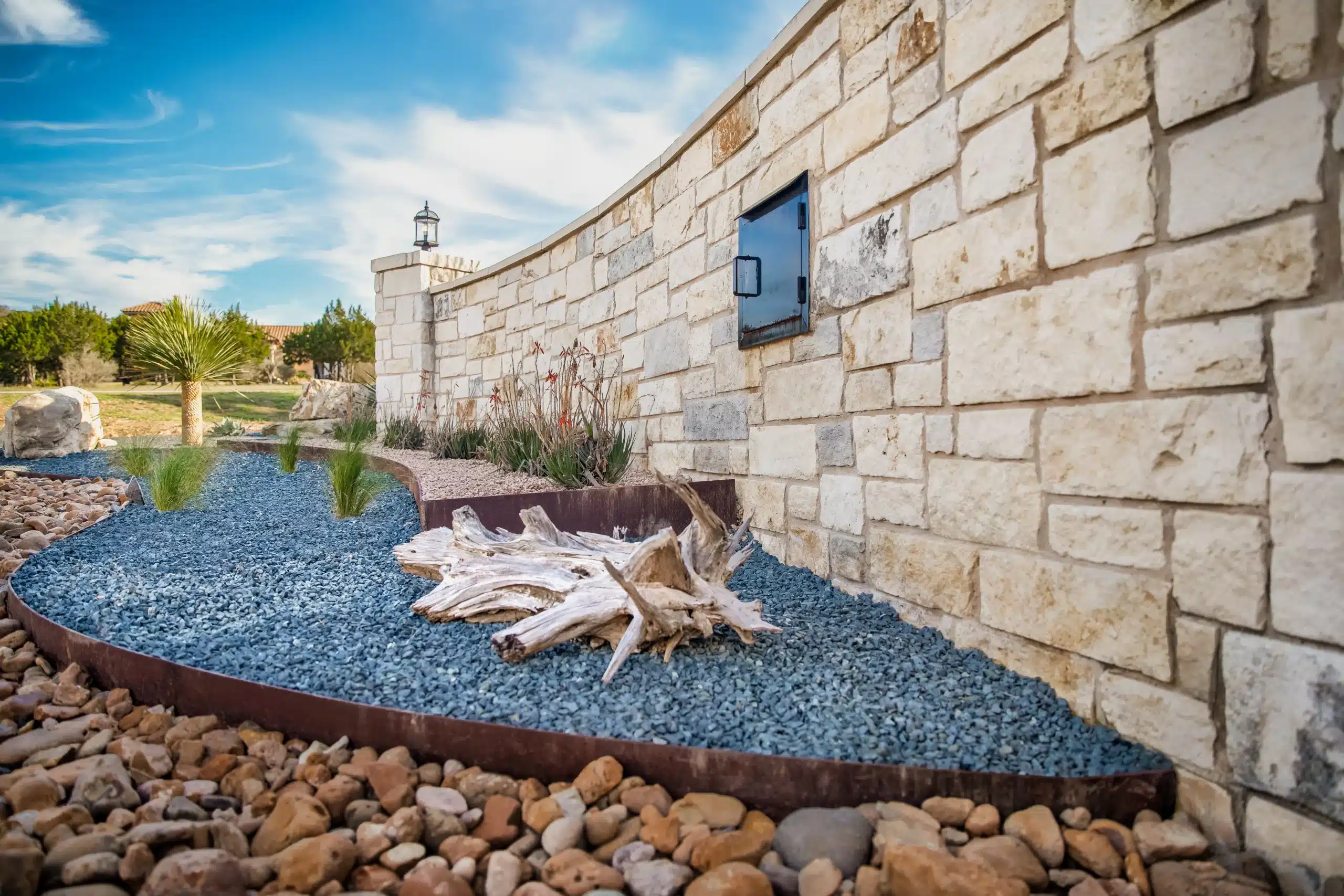 tiered plant beds with natural rock, driftwood, and Texas-native plants along rock wall