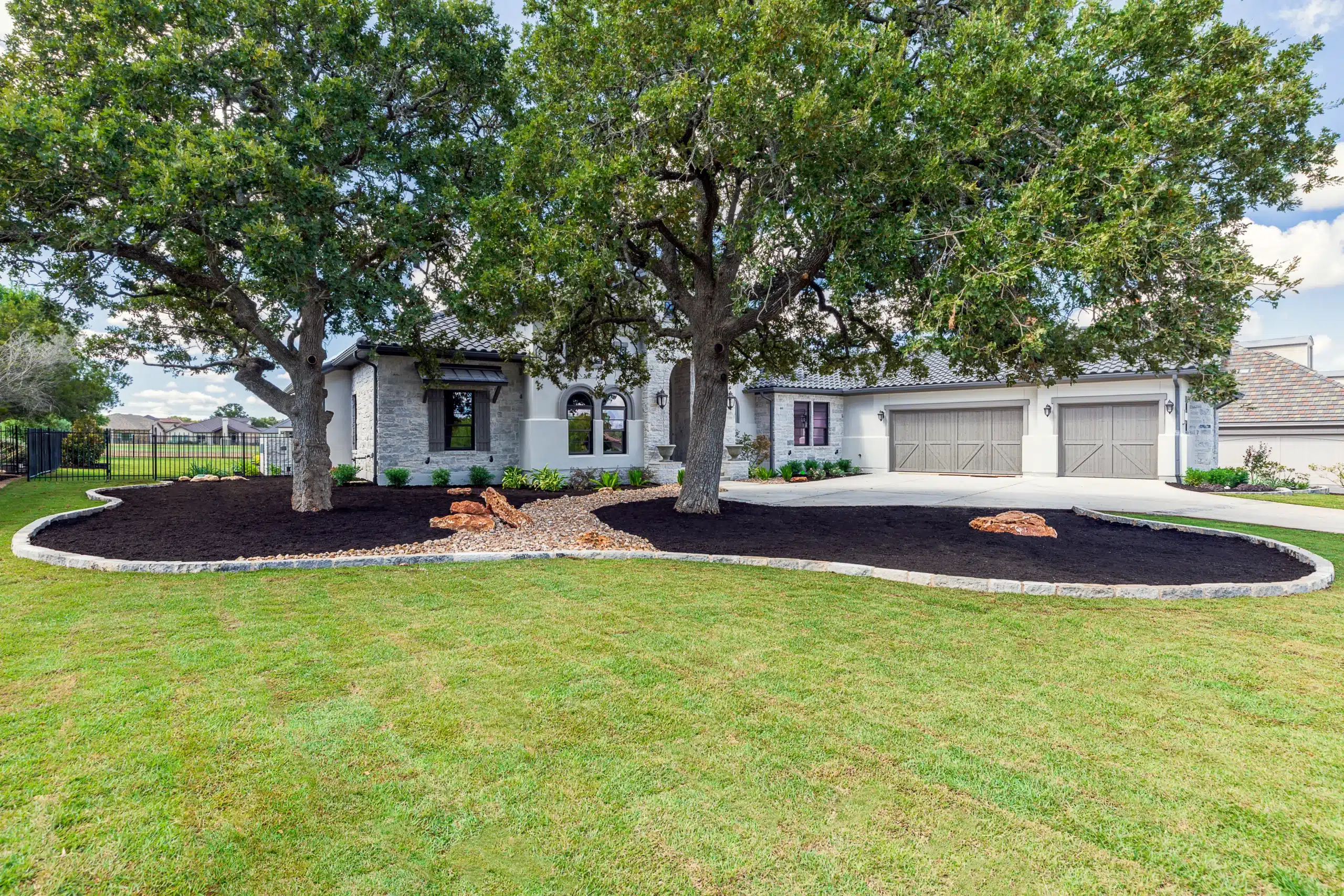 large rock and planter beds around trees in front yard of large home with white rock