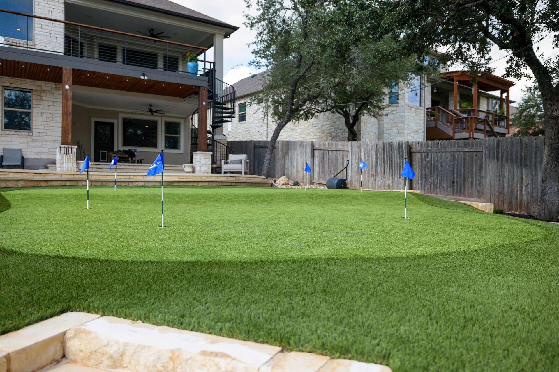 backyard landscape design with mini golf putting green in fenced yard behind two story home with multi-level deck and spiral staircase