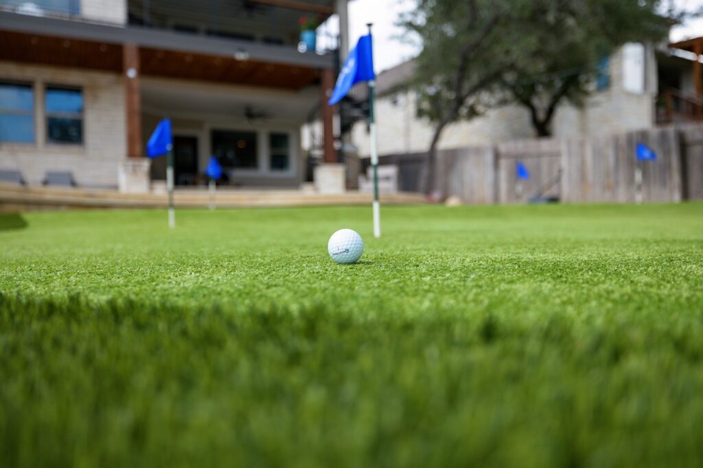 closeup of golfball on putting green in homeowner's backyard with stakes scattered around holding up blue flags
