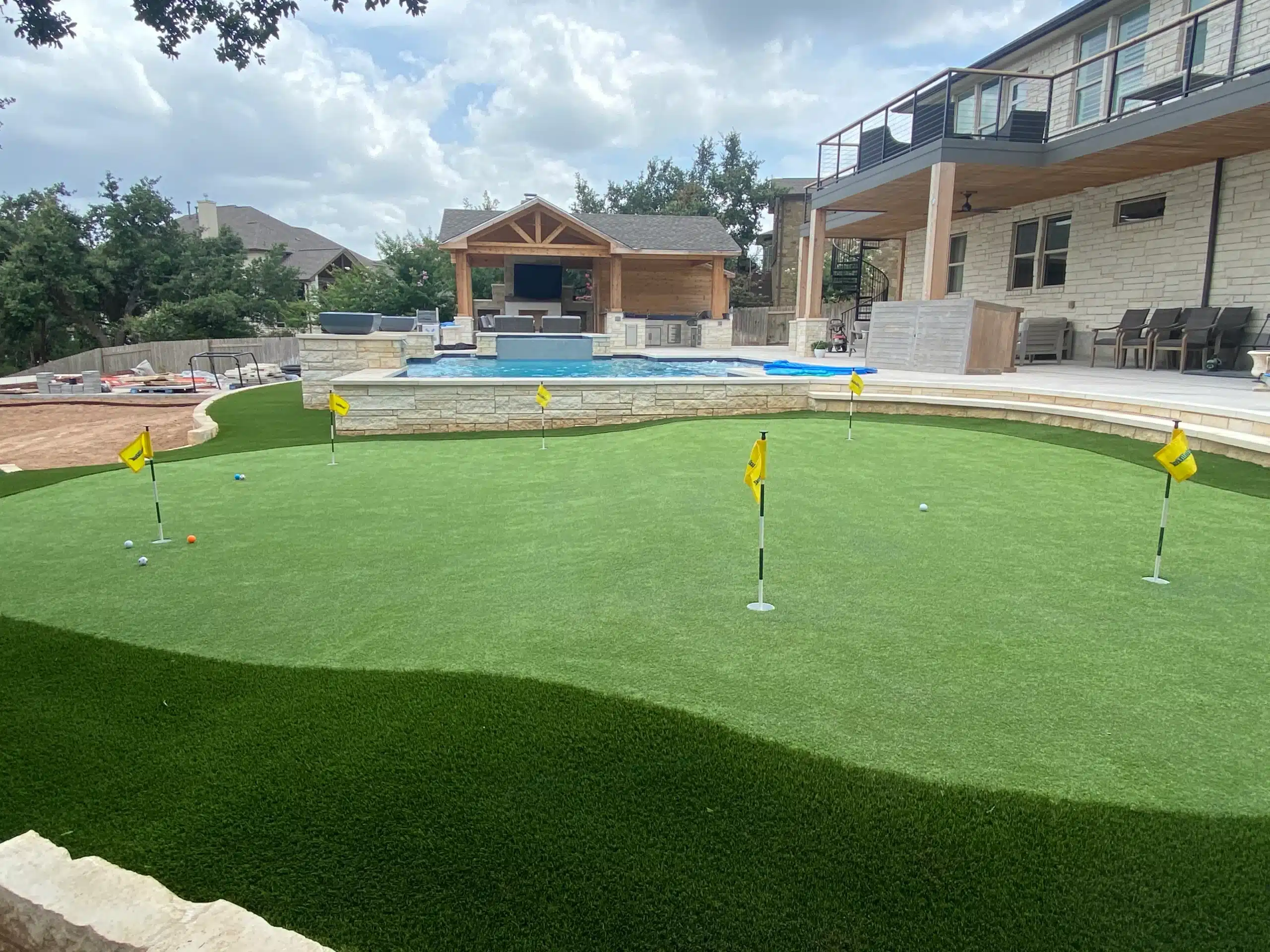 mini golf course next to in-ground pool in the backyard of two story home outfitted with small pool house