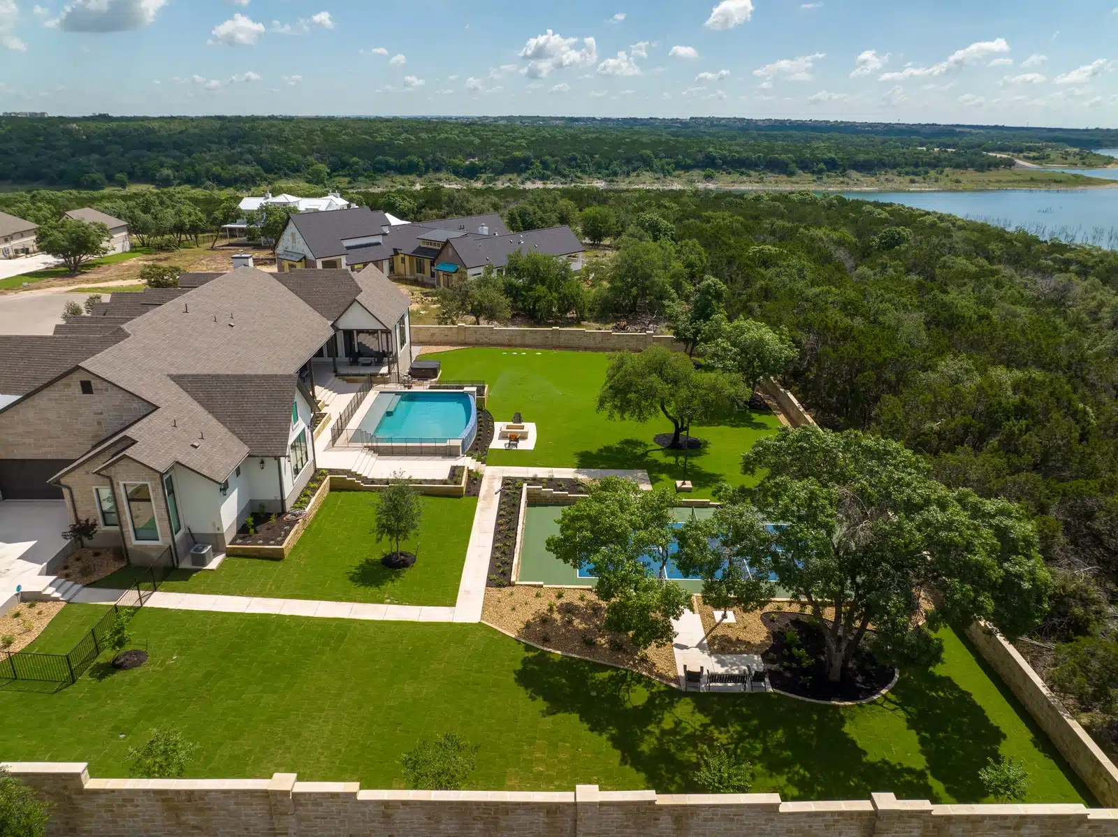 aerial view of Georgetown, Texas home near the lake with trees surrounding a backyard with a pool, tennis court, seating area and fire pit