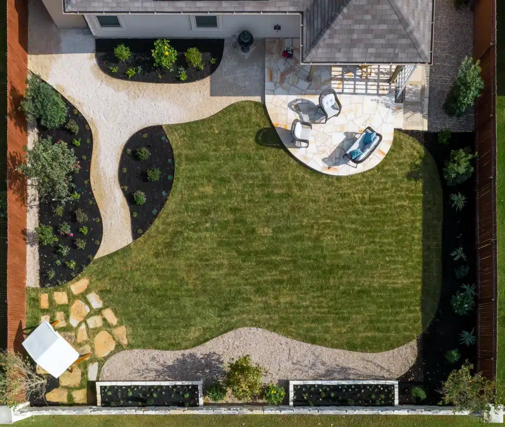 aerial view of square backyard with patio extension and lawn lined with mulch plant beds, raised rock planters, and walkways leading to different areas