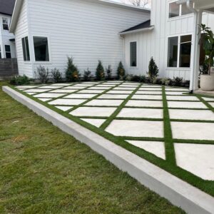 Turf Squares overlayed on large concrete patio extension with landscaping along edges behind a white house
