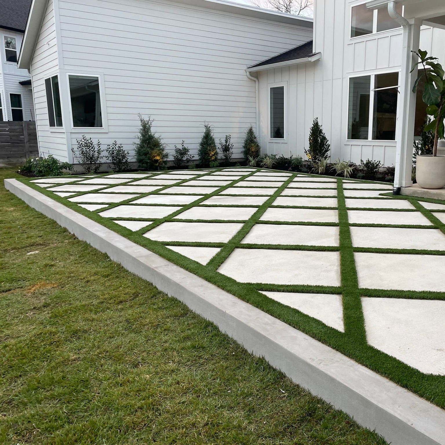 Turf Squares overlayed on large concrete patio extension with landscaping along edges behind a white house