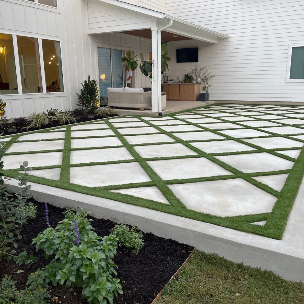 Backyard patio extension with turf squares and landscaped edge behind a white house