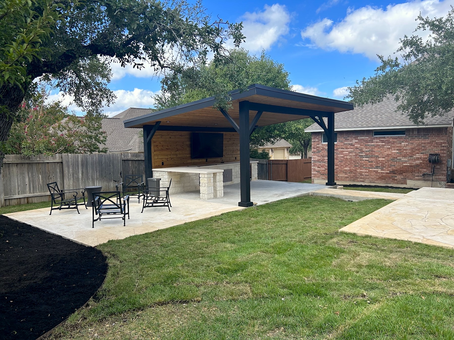 backyard patio with shade cover with an outdoor kitchen of white rock, bar top, and outdoor tv