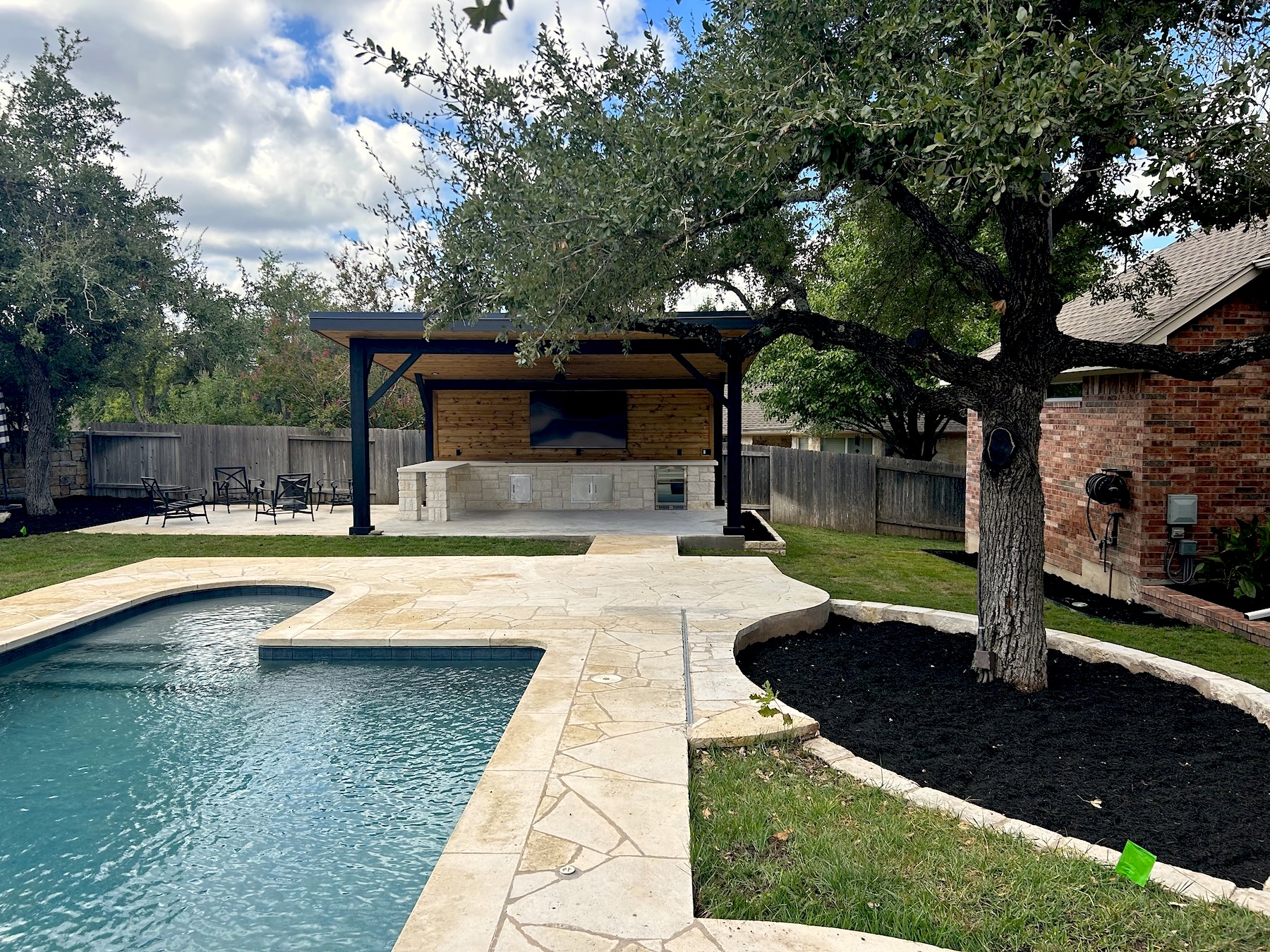 backyard outdoor living space overlooking pool with shade cover, outdoor kitchen, bar top, and raised plant beds